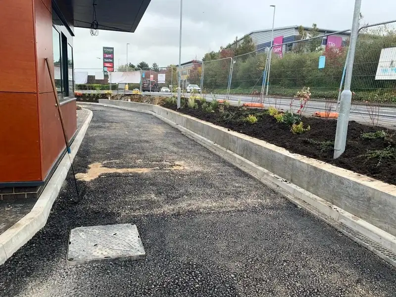 New tarmac path with concrete kerbs and a channel drain beside a planted bed