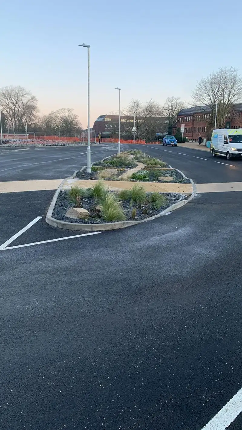 Newly surfaced car park with a kerbed planting island and white bay markings